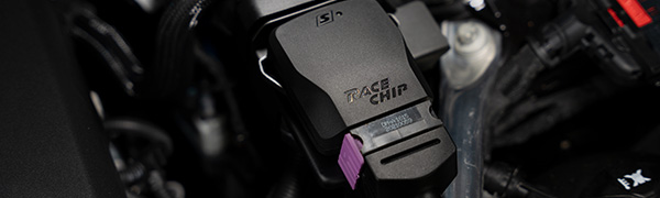 Gros plan du boîtier RaceChip S dans un compartiment moteur, boîtier noir avec logo RaceChip, étiquette produit et connecteur d'origine violet.